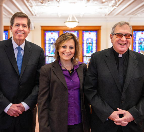 Un groupe de cinq personnes se tient ensemble dans un couloir d’hôpital bien éclairé, en souriant à l’objectif. Deux portent un stéthoscope et des vêtements médicaux, une porte un sweat à capuche de l’université Gonzaga, et les autres sont vêtus de vêtements décontractés ou professionnels, représentant un mélange d’étudiants et de professionnels de la santé.